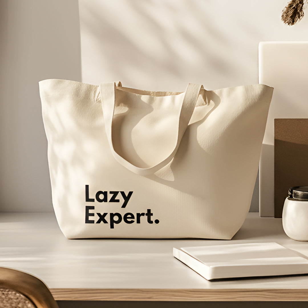 Off-white canvas tote bag printed with the words "Lazy Expert." resting on a bright wooden tabletop next to a notebook.