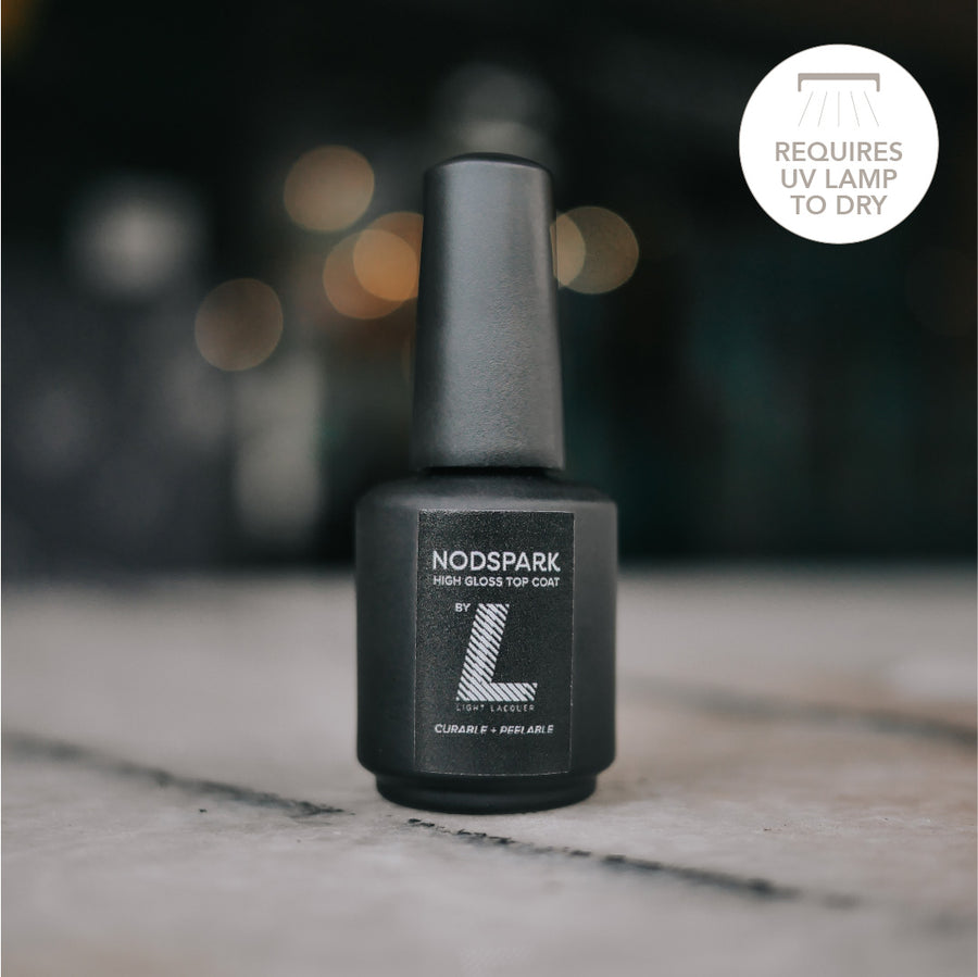 Matte black bottle of Light Lacquer peel-off gel top coat standing upright on a soft-focus background.