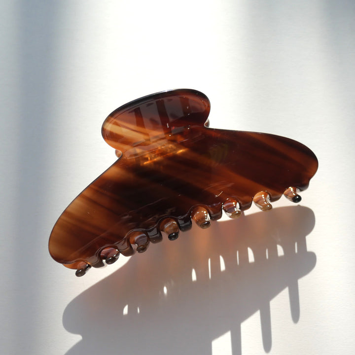 Tortoiseshell brown classic curved hair claw clip casting a shadow on a white surface.