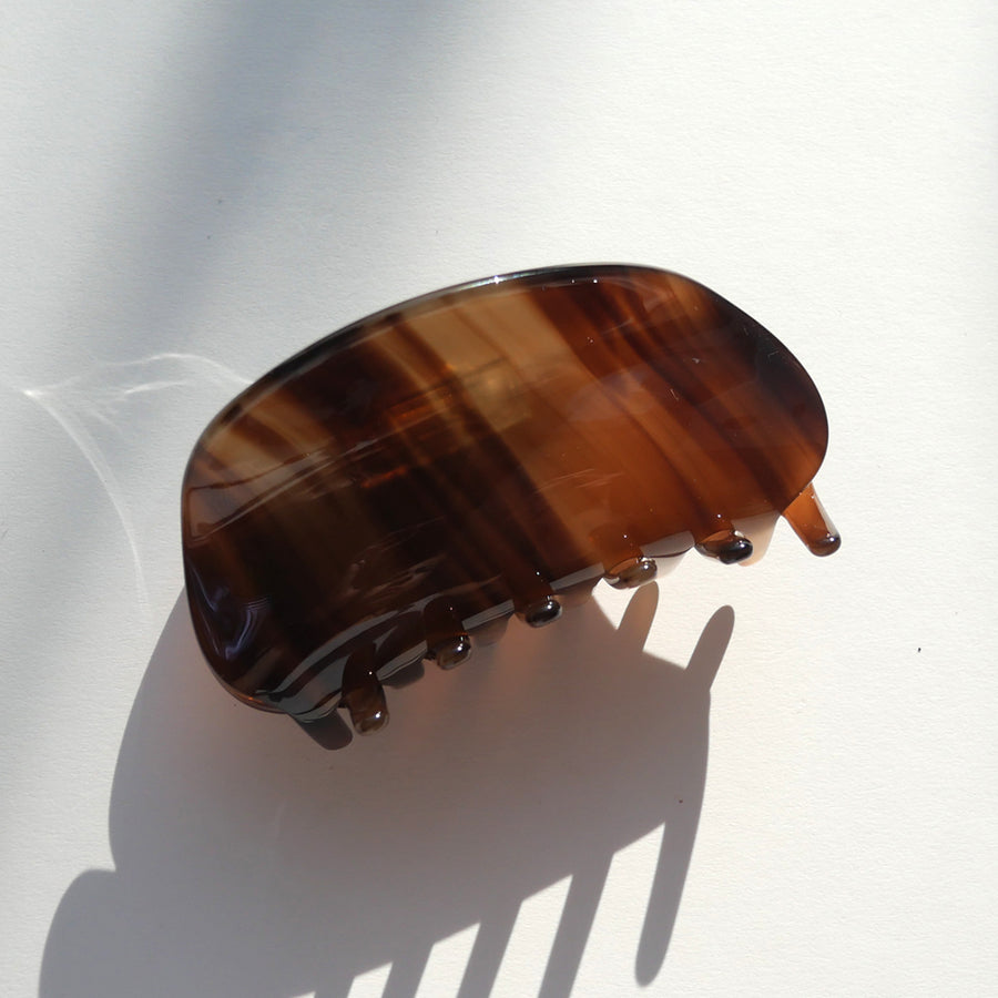 Tortoiseshell brown conch-shaped hair claw clip angled upward, casting a shadow on a smooth white background.