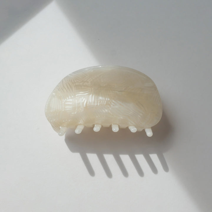 Milky white conch-shaped hair claw clip resting on a light surface with soft lighting.