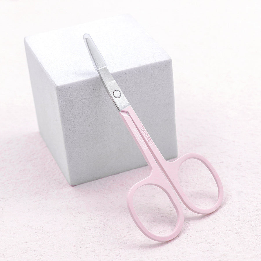 Light pink precision beauty scissors resting angled against a white pedestal block.