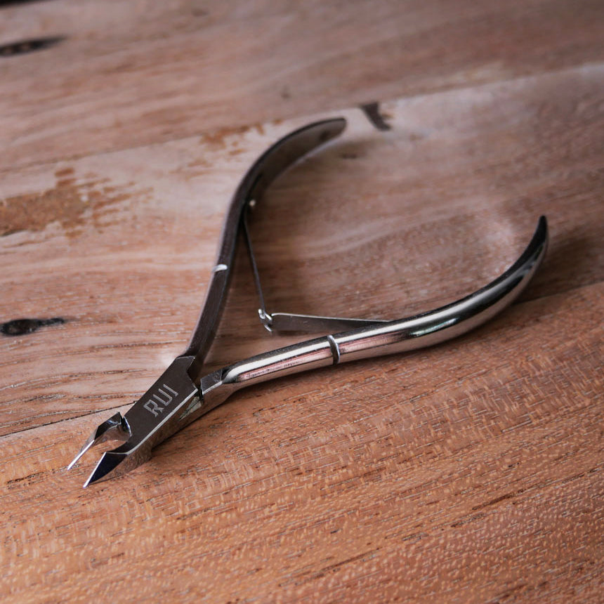 Stainless steel cuticle nippers lying flat on a textured wooden background.