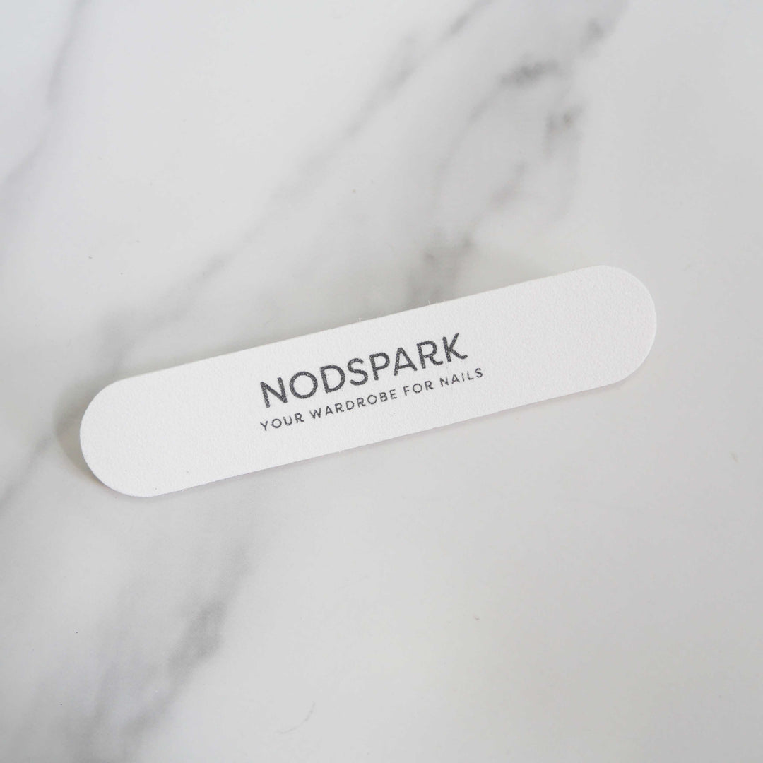 White disposable Nodspark nail file lying diagonally on a smooth marble surface.