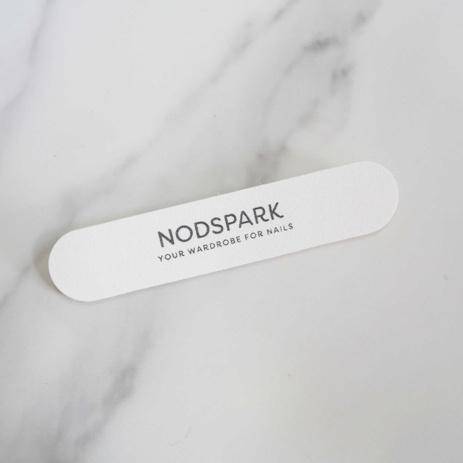 White disposable Nodspark nail file lying diagonally on a smooth marble surface.