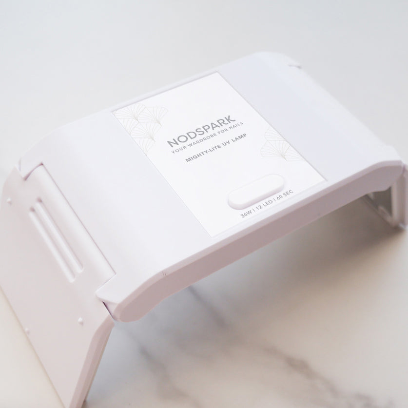 Compact white foldable UV LED nail lamp with extended side legs shown resting on a smooth surface.