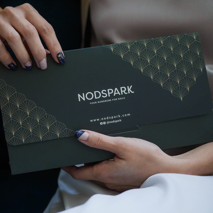 Hands holding an elegant dark green Nodspark gift envelope with a gold geometric pattern design.