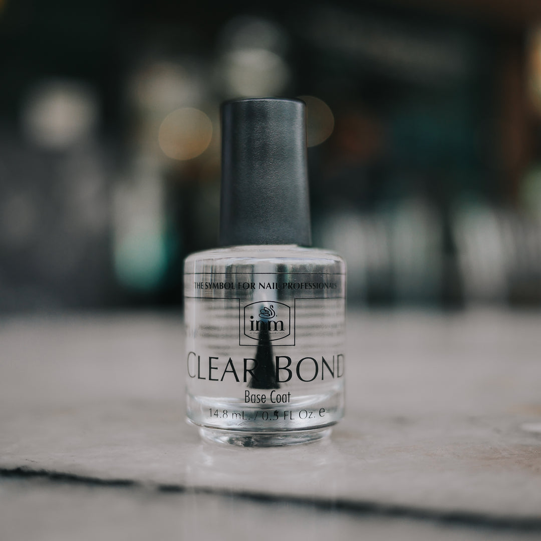 Clear bottle of INM Clear Bond base coat with a black cap standing upright on a marble counter.