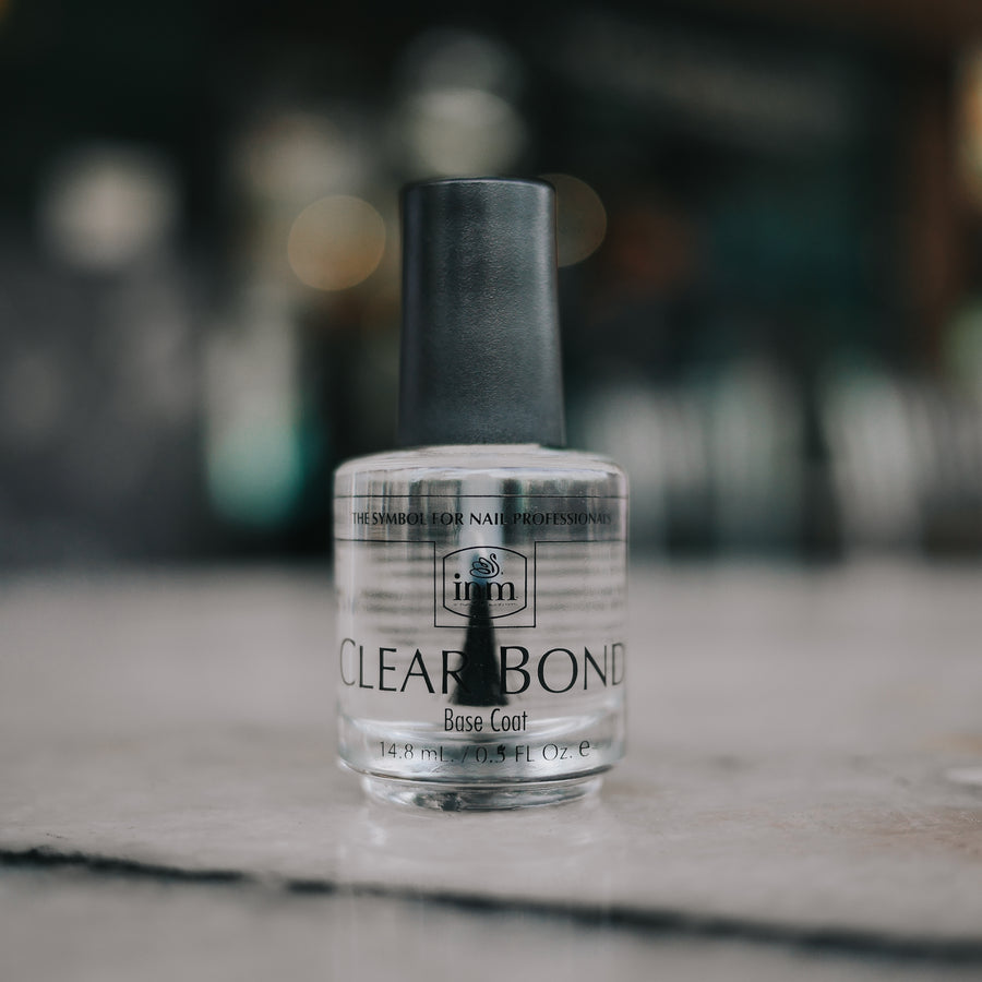 Clear bottle of INM Clear Bond base coat with a black cap standing upright on a marble counter.