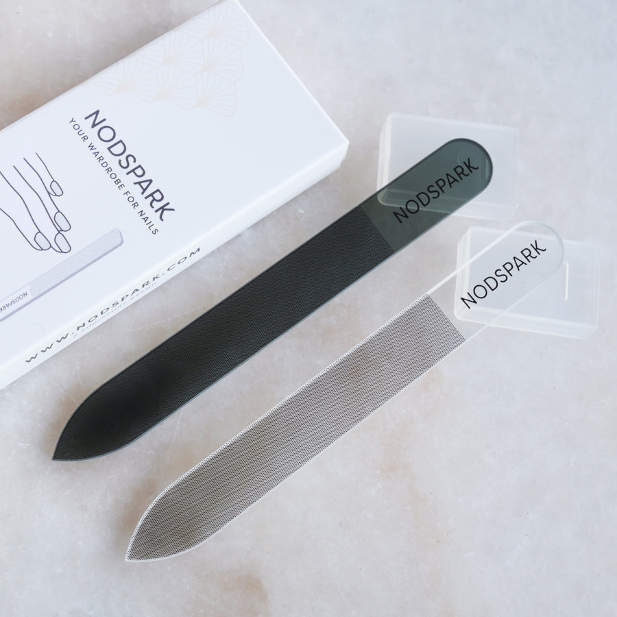 Two sleek nano glass nail files with protective branding sleeves displayed on a light marble surface.